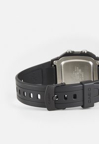 Montre de sport en résine noire avec finition mate, bracelet ajustable et dos en acier inoxydable. Présente plusieurs trous pour ajuster le bracelet.