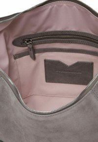 Grijze suède handtas interieur met een gladde roze voering, voorzien van een zak met rits en een geborduurd merkembleem. De randen zijn netjes gestikt.