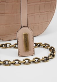 Sac à main beige à texture crocodile avec une étiquette dorée "River Island" et une épaisse chaine en or ancien sur fond blanc.