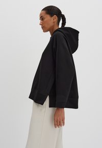 Felpa nera con cappuccio, dal taglio rilassato, con polsini e fondo a coste e design con spacco laterale. Realizzata in morbido tessuto misto cotone.