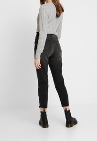 Gray cable-knit sweater with long sleeves, paired with high-waisted black denim pants. Black ankle boots with a loop detail on the heel.