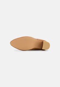 Zapato de tacón marrón con punta afilada, hecho de cuero suave. La suela es beige con un agarre texturizado y un tacón bajo. 