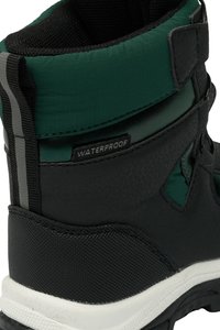 Black waterproof boot with green accents, textured material, reinforced heel, and visible stitching. Features gray stripes for added detail.