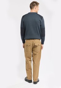 Dunkelblauer gerippter Pullover mit schwarzen Schulterpatches, kombiniert mit hellbraunen Cargo-Hosen mit Gesäßtaschen und geradem Bein.