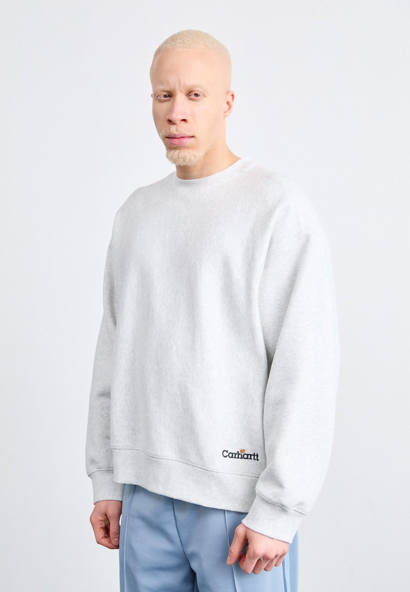 Sweatshirt gris à col rond avec des manches longues et des poignets côtelés. Présente un logo brodé discret dans le coin inférieur. Texture lisse et douce.