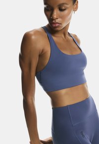 Sujetador deportivo azul claro con escote redondeado y tirantes anchos, hecho de material elástico. Combinado con leggings a juego de cintura alta.