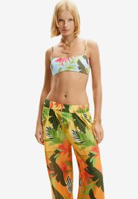 Dwuczęściowy strój składający się z niebieskiego bikini w kwiaty z cienkimi ramiączkami oraz luźnych spodni w tropikalny wzór w kolorach żółtym, zielonym i pomarańczowym.