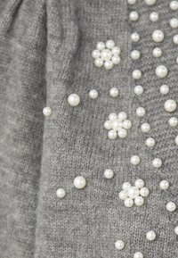 Tessuto a maglia grigio con perle finte bianche di diverse dimensioni sparse, creando un motivo testurizzato su tutta la superficie.