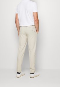 Beiga byxor i lättviktsmaterial med rak passform och bakfickor. Bärs med en vit t-shirt och vita sneakers.