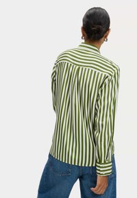Camicia a righe verdi e bianche con maniche lunghe, colletto a punta e polsini con bottoni. Il tessuto appare liscio e leggero.