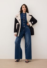 Denimowy strój składający się z dużego, ciemnoniebieskiego płaszcza z kremowymi akcentami z futra, dopasowanej kurtki z guzikami oraz spodni o szerokich nogawkach.