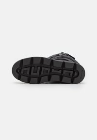 Botte d'hiver noire posée sur le côté montrant la semelle rainurée avec des crampons profonds et un petit logo de marque sur le talon.