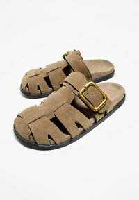 Rjave suede sandale z več izrezi, prilagodljiv trak z zlatim zaponko in črn gumijast podplat za oprijem.