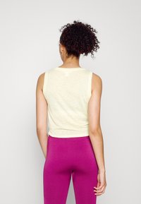 Top cropped amarelo claro, sem mangas, com uma textura suave. Combinado com leggings roxas ajustadas e elásticas, apresentando detalhe canelado.