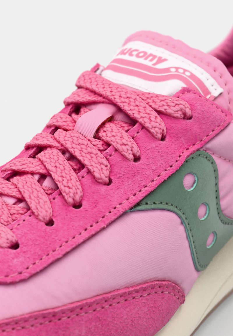 Różowe sneakersy z połączenia zamszu i materiałów tekstylnych, z różowymi sznurowadłami, zielonym akcentem logo oraz gładką podeszwą.