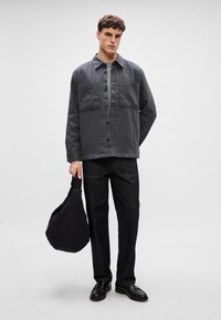 Szürke csíkos gombos ing, két mellzsebbel, sötét farmernadrággal párosítva. A modell egy fekete steppelt táskát tart, és cipőt visel.