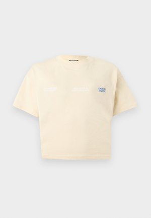 Bézs színű, rövid ujjú, rövid fazonú póló, melyen kis fehér és kék feliratok olvashatók: "Engineered for Speed", "Precision & Performance" és "On The Track".