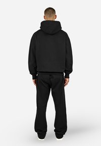 Camisola com capuz preta e calças de fato de treino a condizer, feitas de tecido macio, com capuz grande, corte relaxado e punhos elásticos nos pulsos e na cintura.