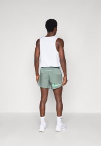 Conjunto deportivo masculino que incluye una camiseta sin mangas blanca y shorts verdes con el logo de Nike en blanco y verde, complementado con calcetines y zapatos blancos.