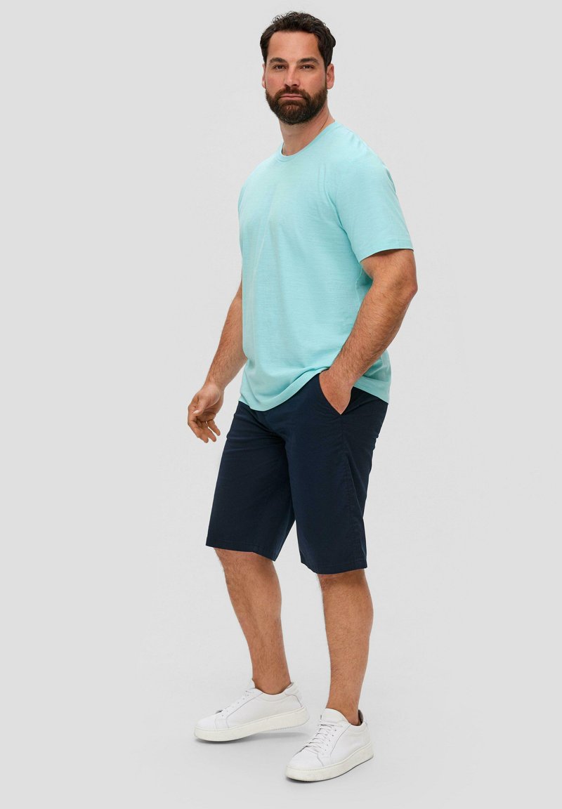 Lichtblauw shirt met korte mouwen, gecombineerd met donkerblauwe shorts en witte sneakers. Het shirt heeft een ontspannen pasvorm en een zachte textuur.