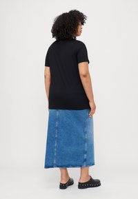 Schwarzes T-Shirt mit kurzen Ärmeln, kombiniert mit einem blauen Jeans-Maxirock, der einen geraden Schnitt und einen ausgefransten Saum aufweist, getragen mit schwarzen Clogs.