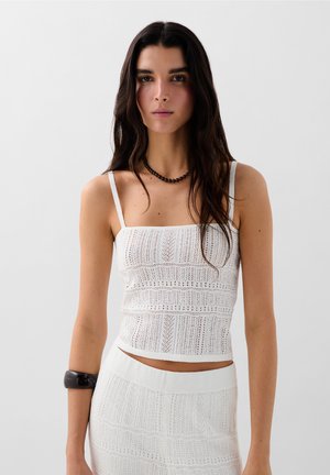 Haut court blanc avec un décolleté carré, des bretelles fines et une texture de tricot délicate. Associé à une jupe assortie taille haute.