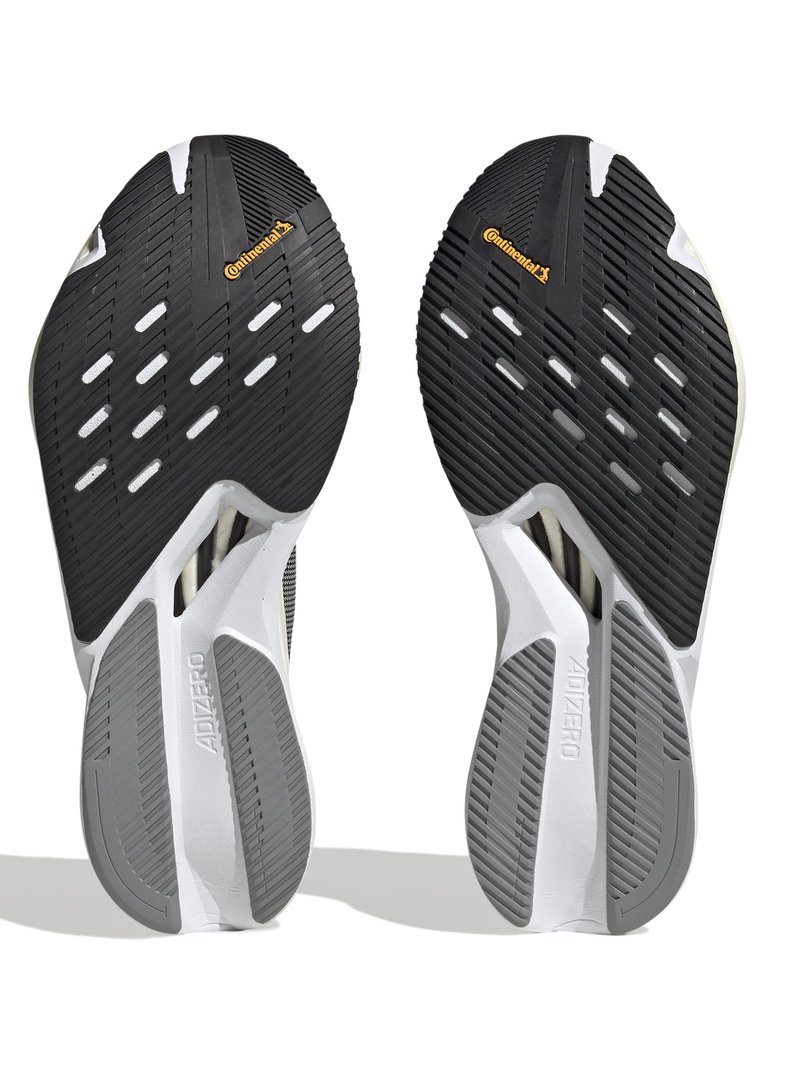 Semelles de chaussures de course noir et blanc avec une surface en caoutchouc texturé, présentant des rainures et un logo Continental en jaune. La semelle a un design léger.
