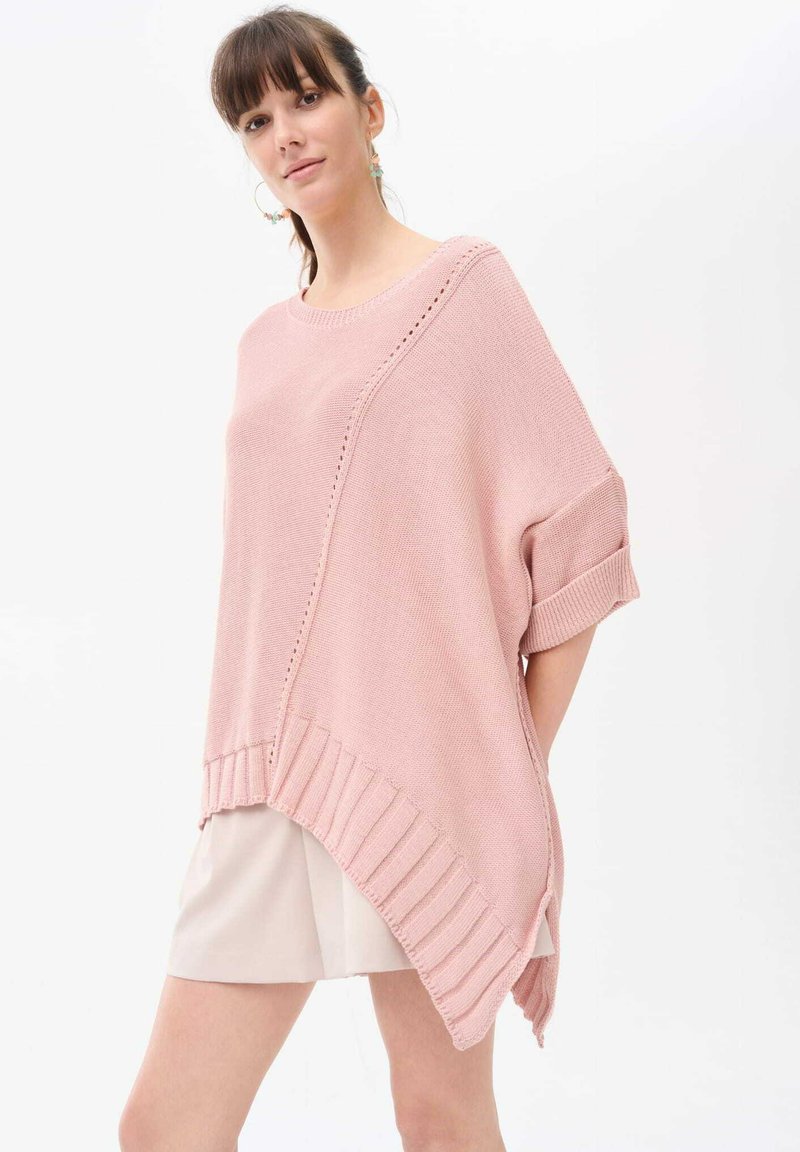 Lichtroze oversized gebreide pullover met geribde rand en opgerolde mouwen. Heeft een diagonale naad en subtiele horizontale textuur.