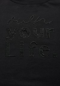 Sudadera de algodón negra con un diseño texturizado y strass negros que dicen "construye tu vida". La tela tiene un acabado suave.