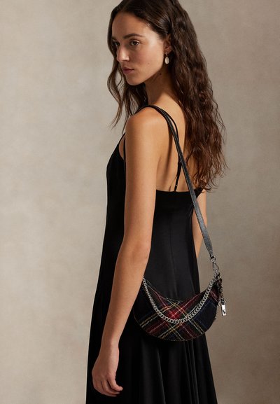 Fekete ujjatlan ruha; a modell egy kockás keresztpántos táskát tart láncos pánttal, amely több színű mintákkal és fényes felülettel rendelkezik.