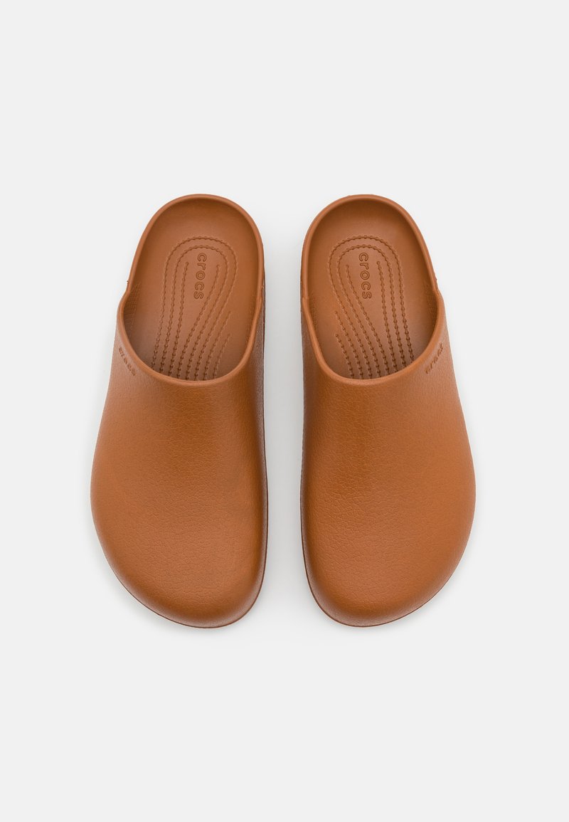 Bruine instapschoenen gemaakt van een gladde, matte stof met een gevormd voetbed en afgeronde randen, voorzien van groeven voor grip aan de binnenkant.