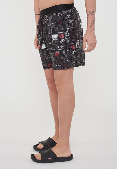 Pantaloni corti neri a fantasia con un cinturino strutturato, caratterizzati da stampe grafiche in rosso, bianco e nero. Abbinati a sandali neri in slide.