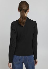 Černý strukturovaný blejzr s dlouhými rukávy a přiléhavým střihem, vyznačující se hladkou texturou a minimalistickým designem. Spárován s modrými džíny.
