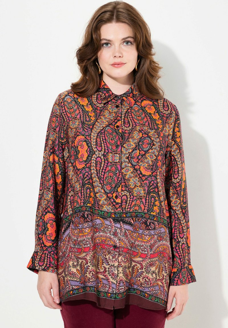 Long-sleeve blouse featuring a vibrant paisley pattern in red, orange, and purple on a dark background. Button-down design with a curved hem.