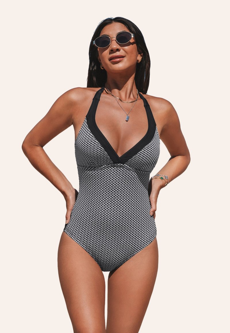 Maillot de bain une pièce à motif noir et blanc avec décolleté en V plongeant, bretelles autour du cou et bord noir uni. Présente un design ajusté.