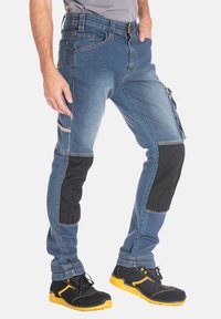 Jeans avec un corps en denim bleu, des accents noirs aux genoux et des poches latérales. Comprend une fermeture éclair et un bouton, ainsi que des détails de couture contrastants.