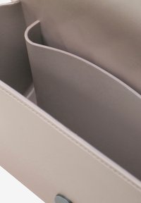 Interno di una borsa color taupe chiaro con una texture liscia, dotata di due scomparti separati da un divisorio curvo e un dettaglio di chiusura circolare.