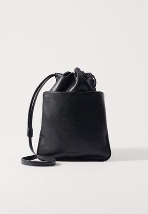 Crna kožna torba u obliku bačve s glatkom teksturom, zatvaranjem na vezicu i dugim remenom za nošenje preko ramena, koja se ističe minimalističkim dizajnerskim detaljima.