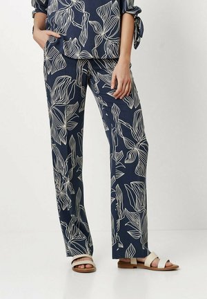 Dunkelblaue Hosen mit einem weißen Blumenmuster, die einen lockeren Schnitt und ein gerades Bein-Design aufweisen. Kombiniert mit hellfarbenen Sandalen.