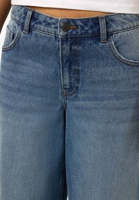 Ανοιχτό μπλε τζιν παντελόνι με ψηλή μέση, κλασικό σχέδιο πέντε τσεπών, αντίθετη ραφή και κλείσιμο με κουμπί μπροστά.