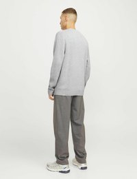 Grauer Pullover mit lässiger Passform, langen Ärmeln und Rundhals, kombiniert mit locker sitzenden grauen Hosen und weißen Turnschuhen.