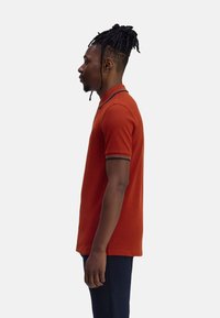 Korte mouwen polohemd voor heren in gebrand oranje, met een contrasterende kraag en manchetten met subtiele strepen. Gladde katoenstof, aansluitend ontwerp.