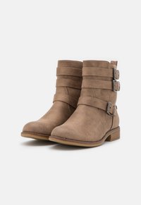 Botas de tobillo de ante color marrón claro con tres correas decorativas, hebillas plateadas, punta redondeada y un tacón bajo apilado. Acabado ligero y texturizado.