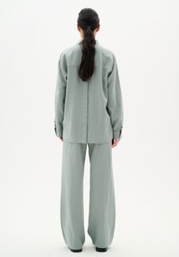 Mintgroene, loszittende shirt en wijde broek van een gestructureerde stof. Het shirt heeft een naad aan de achterkant en knoopmanchetten.