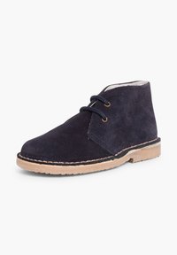 Botín chukka de ante azul marino con dos ojetes, suela de goma beige y costuras a lo largo del borde. Forro interior suave visible.