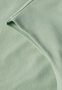 Světlé zelené látka s hladkým povrchem, se skládacími okraji manžet a viditelnými stehy.