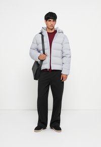 Light gray padded jacket with a hood, front zipper, and elastic cuffs. Worn over a burgundy shirt and paired with black trousers and shoes.