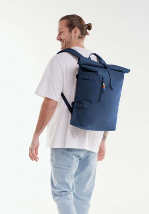 Navyblaue Rolltop-Rucksack mit verstellbaren Trägern, Seitenfach und buntem Reißverschlussanhänger. Hergestellt aus robustem Material, minimalistisches Design.