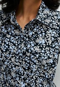 Camicia floreale con una base nera decorata da motivi astratti bianchi e azzurri chiari. Design con colletto, chiusura con bottoni e texture di tessuto morbido.