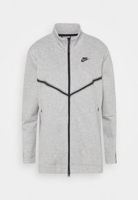 Giacca grigia con zip, realizzata in pile, con colletto alto, dettagli neri e logo Nike sul petto. Presenta tasche laterali con zip.